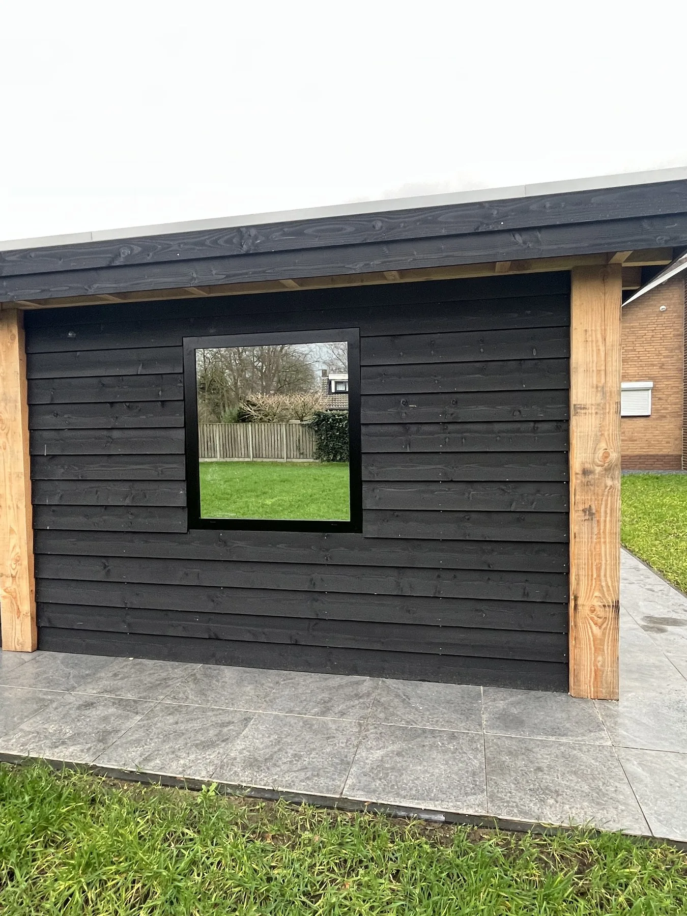 Klein raamkozijn in de zwarthouten gevel van een tuinhuis in Rijsbergen